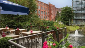 Une terrasse extérieure avec des tables et des chaises, un parasol bleu et un élément décoratif aquatique.