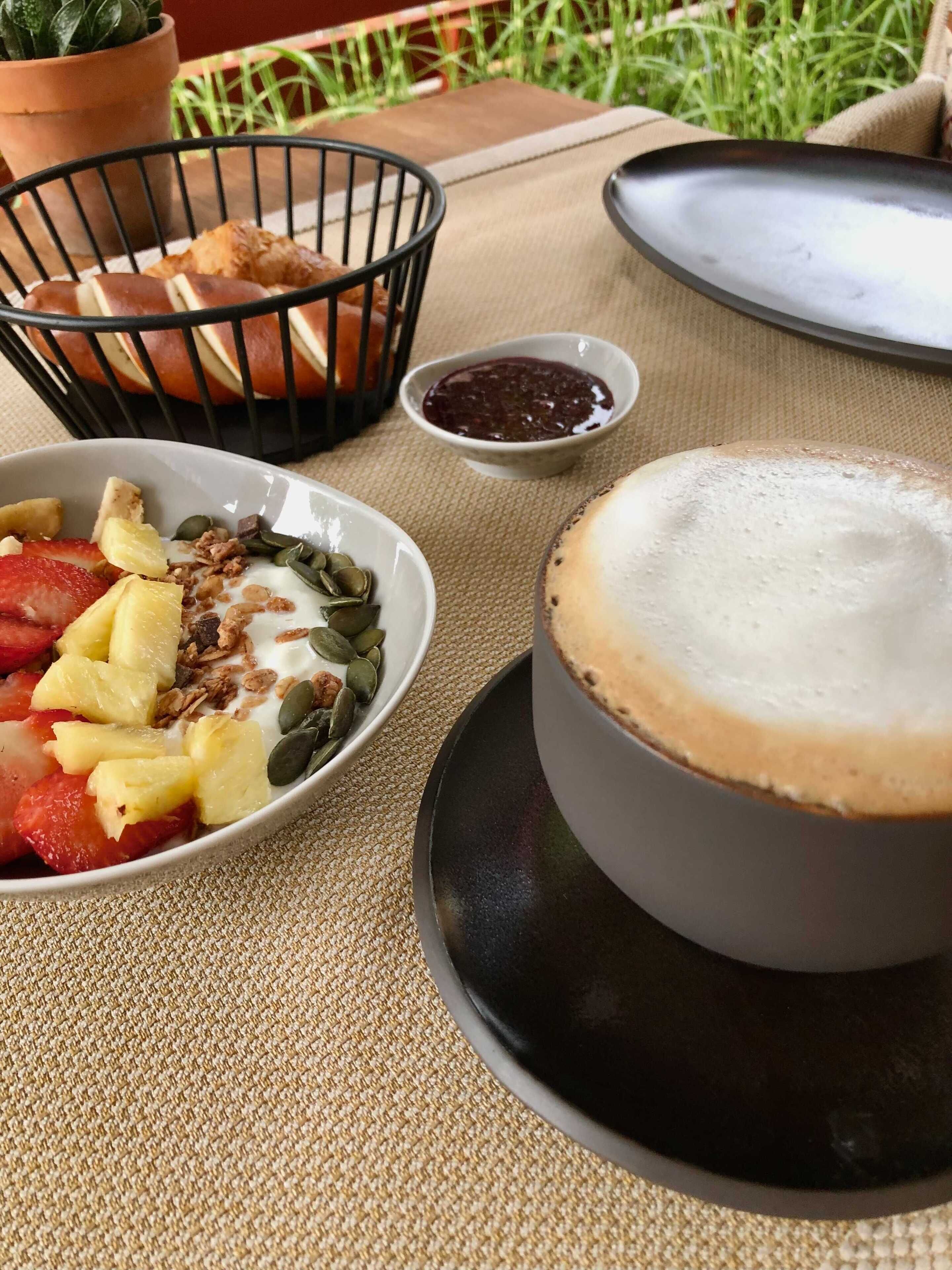 A breakfast setting with a bowl of fruit and granola, a small dish of jam, and a cup of coffee on a table.