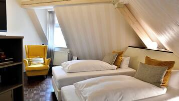 A bedroom with two beds, a yellow armchair, and a wooden ceiling structure.