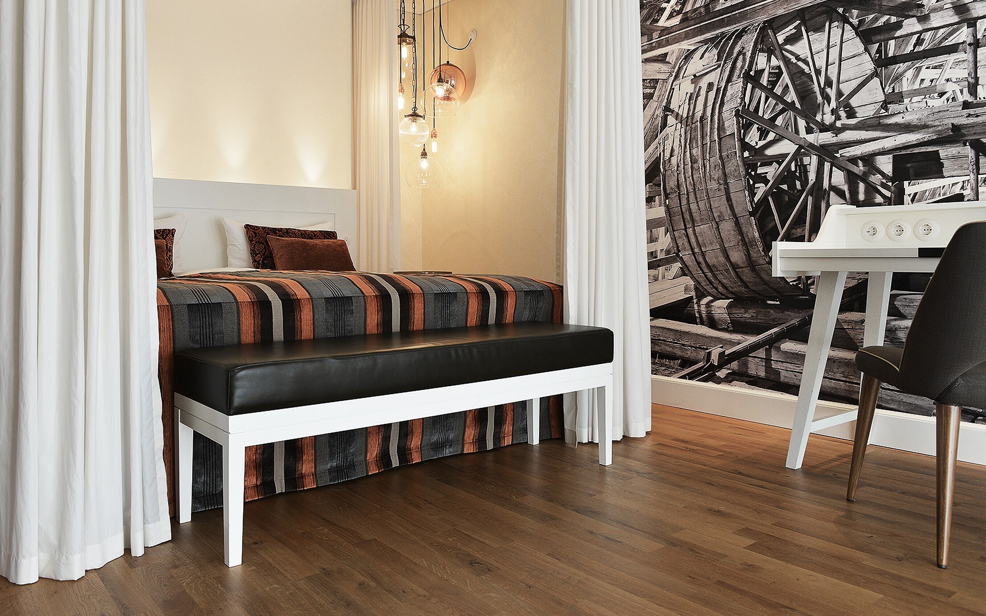 A compact bedroom with a bed, bench, and a small table with a chair.