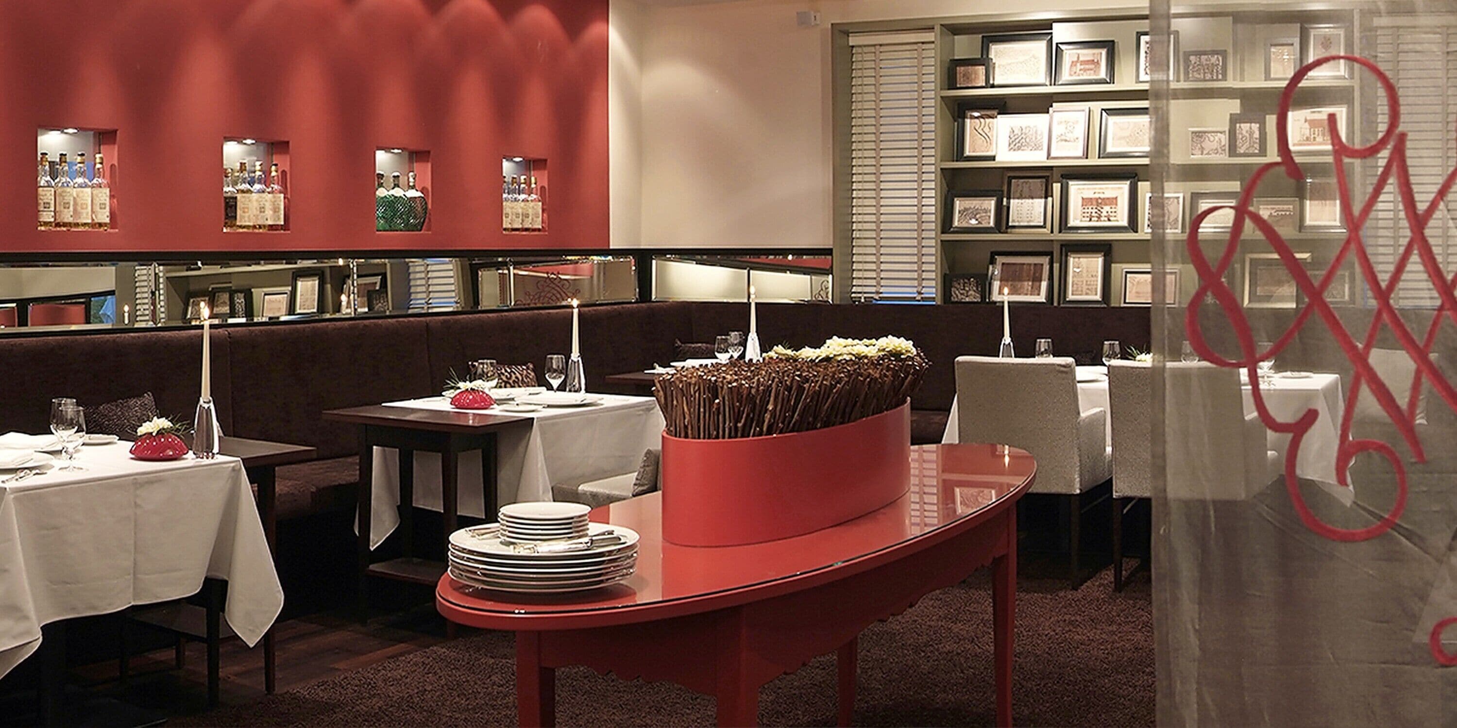 En restaurang med dukade bord, en röd bordsdekoration och inramade tavlor på väggen.