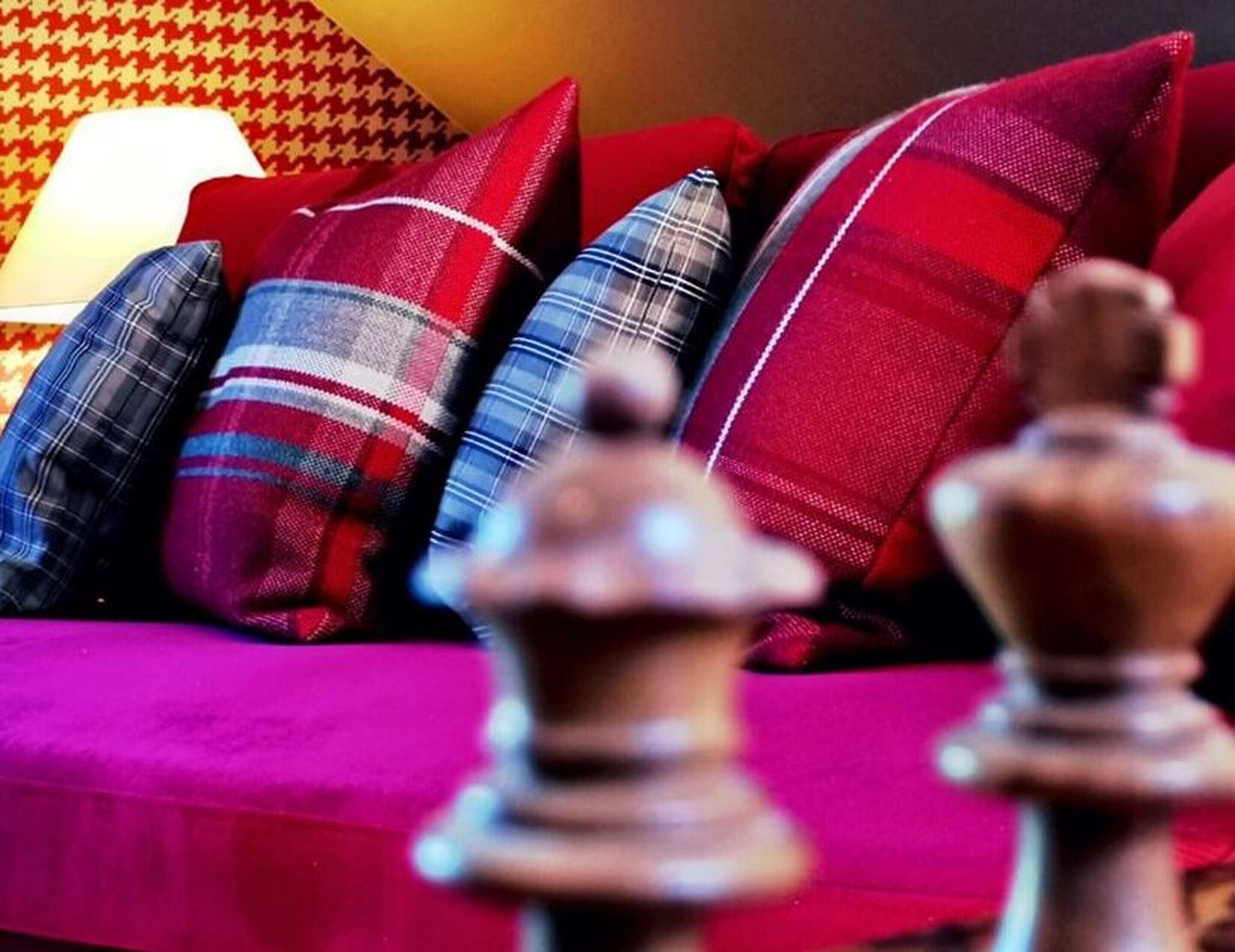 A sofa with plaid cushions and a lamp in the background.
