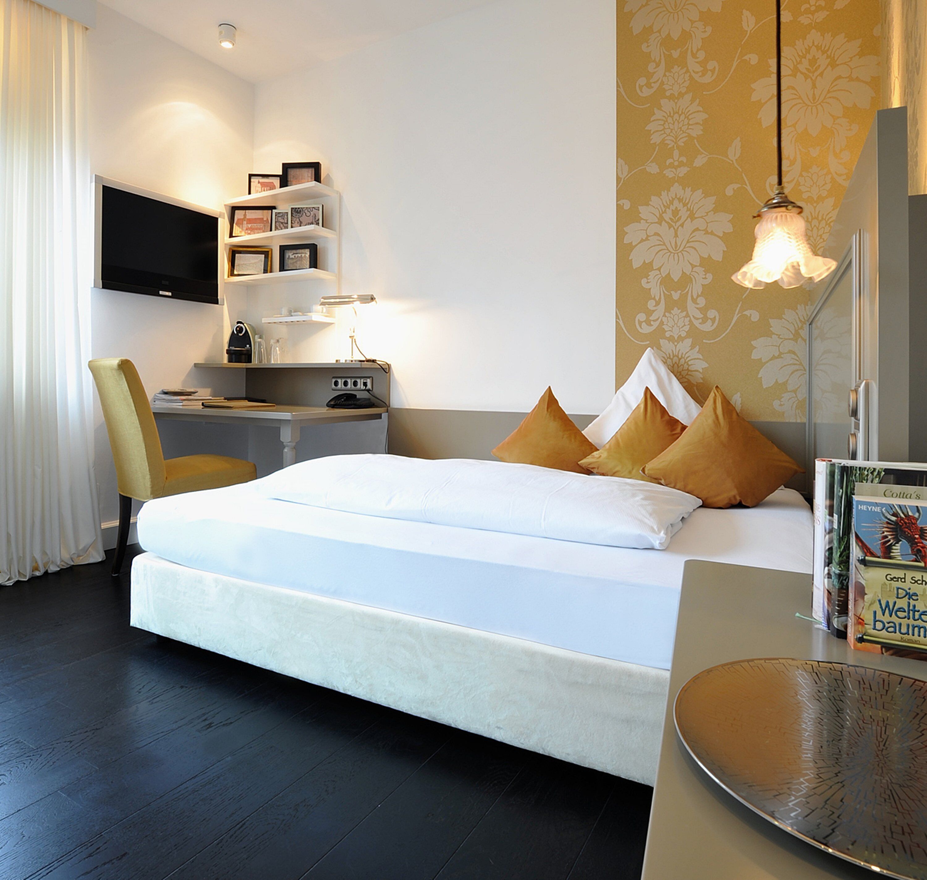 A modern hotel room with a large bed, a desk with a chair, a flat-screen TV, and a bookshelf.