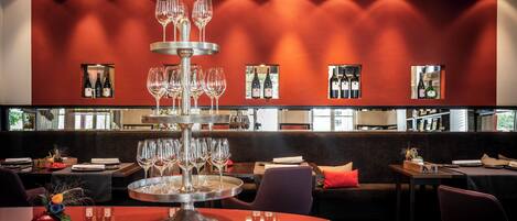 Un restaurante con pared roja, una vitrina de vinos y una mesa redonda con copas.