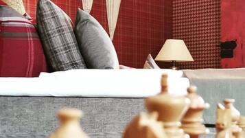 A chessboard with wooden pieces in focus, a sofa with a plaid blanket and pillows, and a lamp on a table.