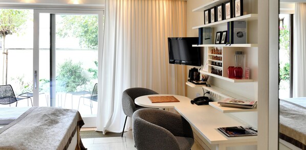 A hotel room with a bed, a desk with a computer, a TV, and a bookshelf.