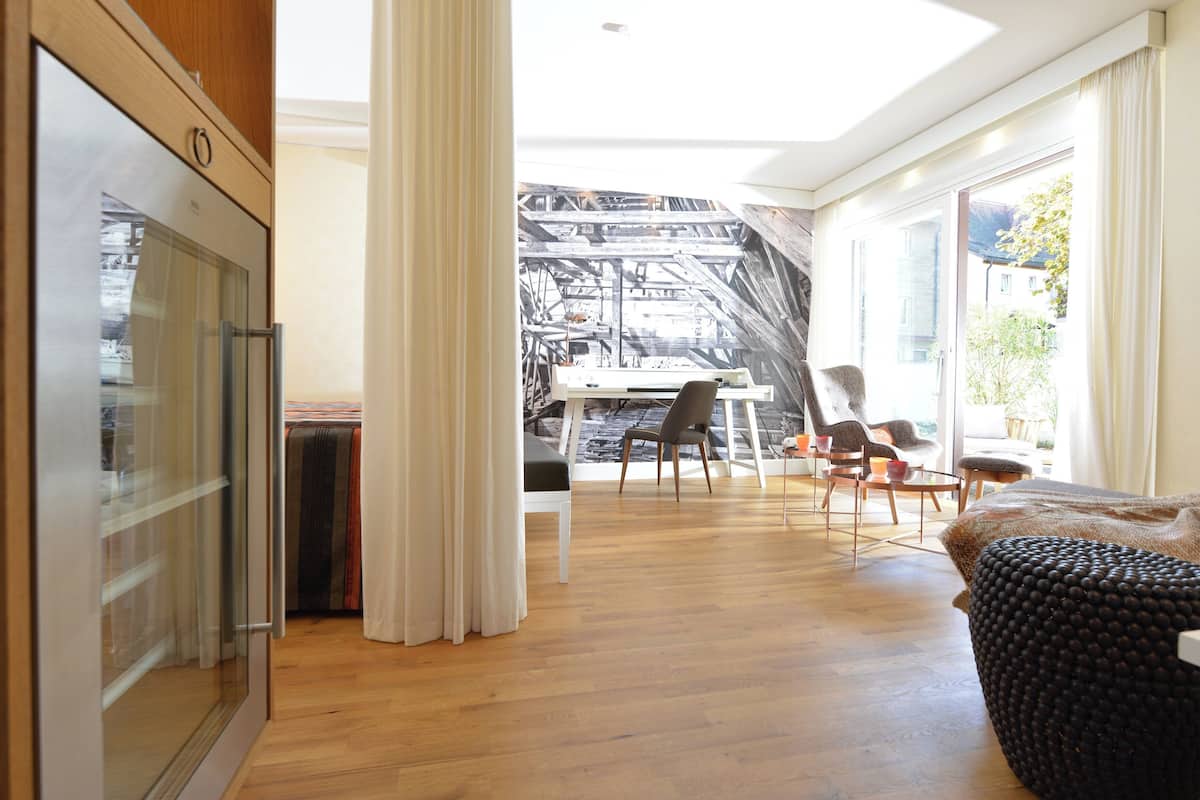 Un interior moderno con suelo de madera, una zona de comedor con sillas, un sofá y vistas a un edificio a través de una ventana.