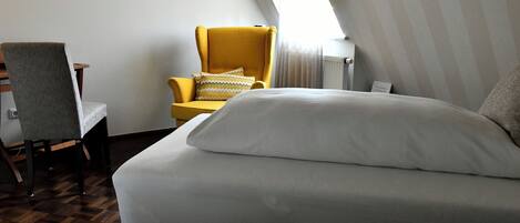 A hotel room with a bed, a chair, and a window.