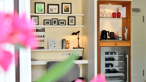 Quarto de hotel com escrivaninha, prateleiras com fotografias emolduradas, luminária e minibar.
