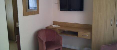 A hotel room with a bed, a desk with a chair, a television, and a wardrobe.