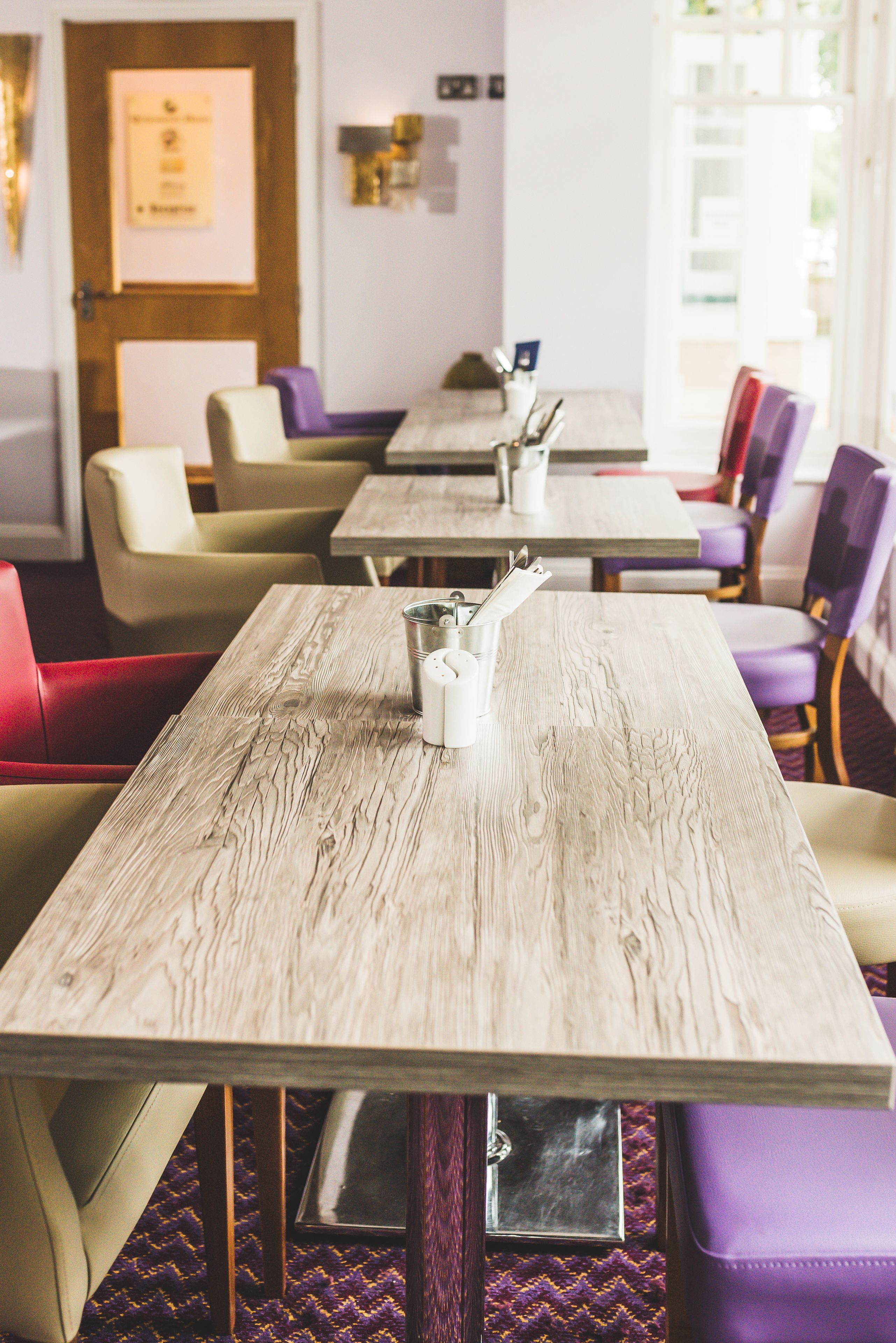 A restaurant with wooden tables and purple and beige chairs.