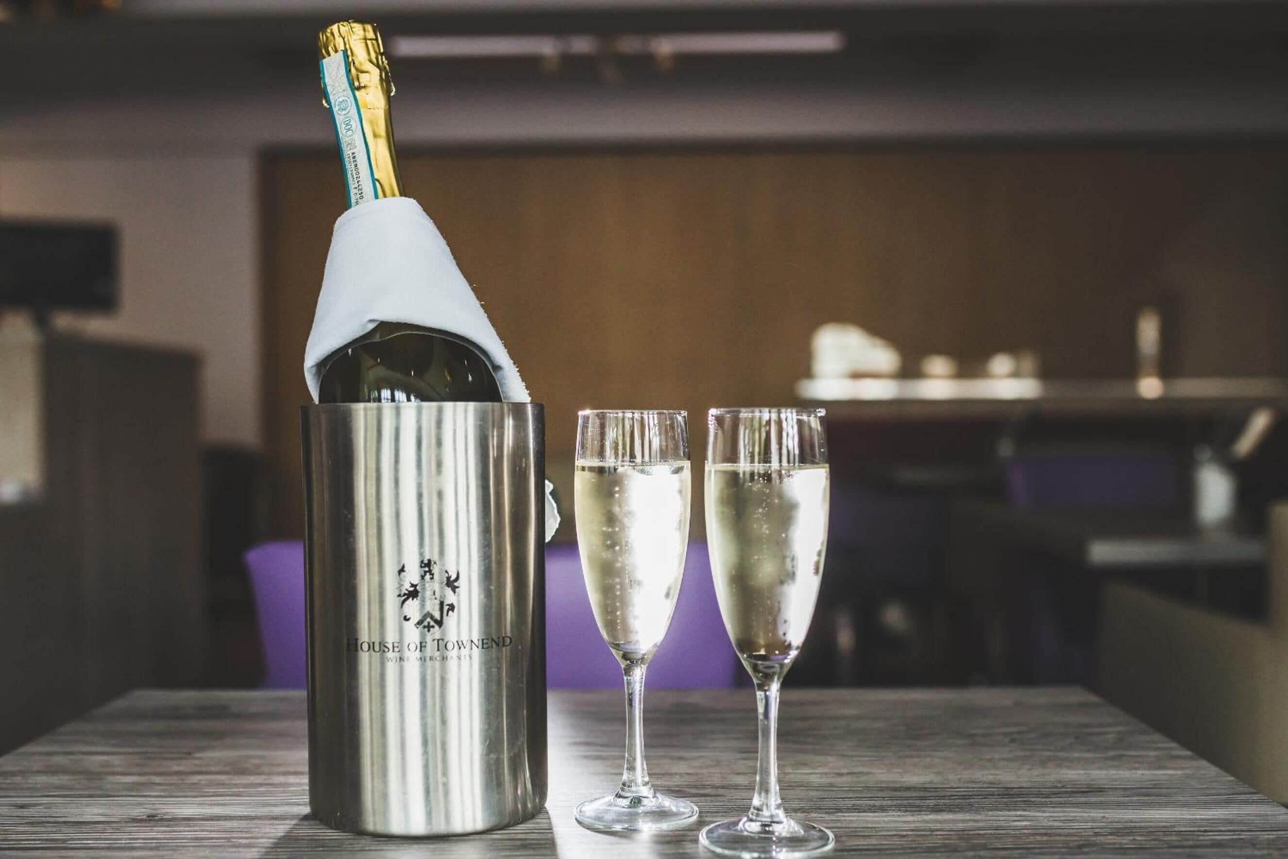 A bottle of champagne with two glasses on a wooden table.