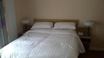 A neatly made bed with white linens, two bedside lamps, and a nightstand with a phone and a lamp.