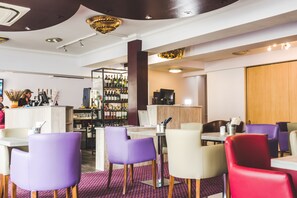 A restaurant with purple and red chairs, a bar area with bottles, and a television. - Queensgate Hotel (Peterborough)