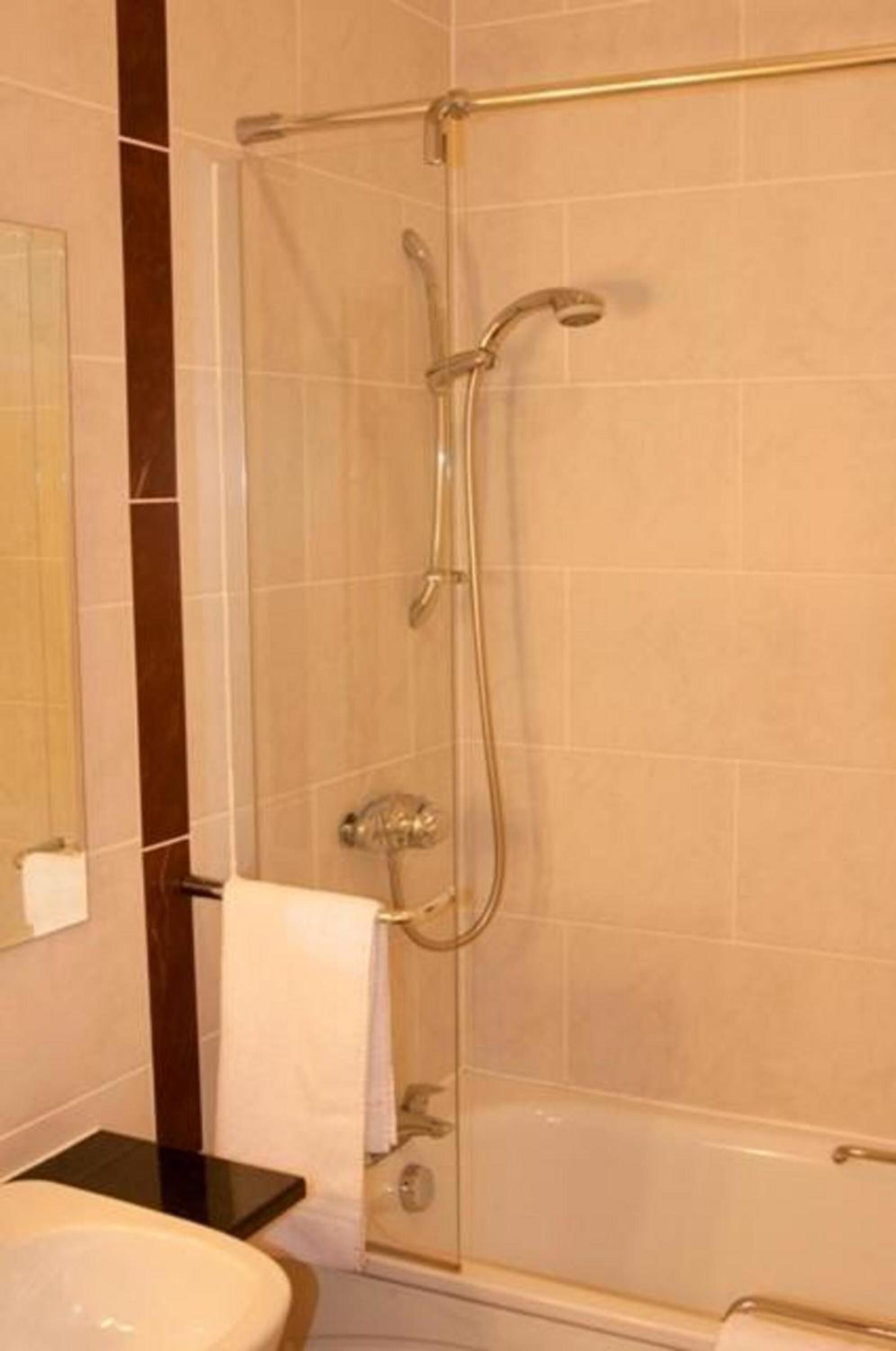 Un baño moderno con ducha de vidrio, lavamanos blanco y encimera oscura.