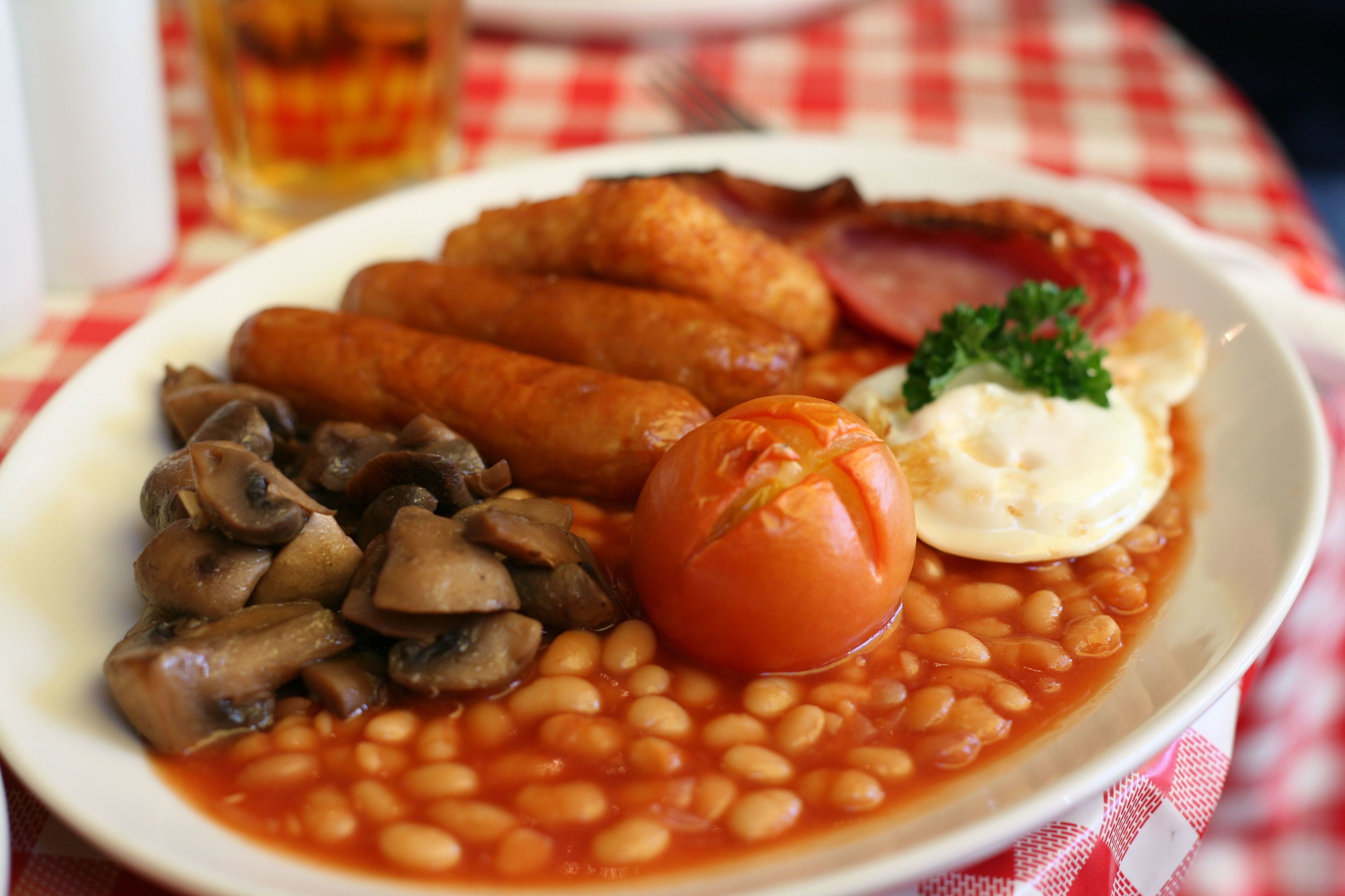 A plate of beans, mushrooms, sausages, a boiled egg, and bacon.
