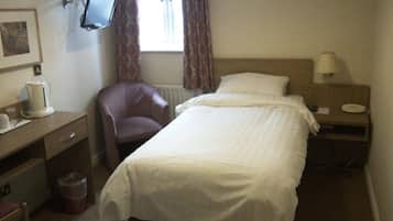 Una habitación de hotel con cama, un escritorio con monitor de ordenador, una silla, una mesita de noche con lámpara y una ventana con cortinas.