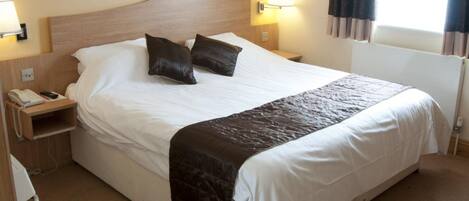 Een net opgemaakt bed met een houten hoofdbord, twee bedlampen en een telefoon op het nachtkastje.