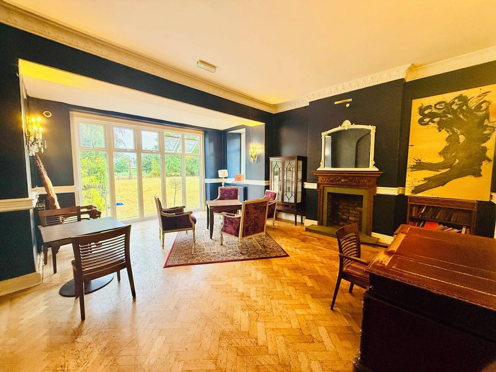 Een ruime woonkamer met een open haard, een eethoek en een groot raam met uitzicht op het landschap.
