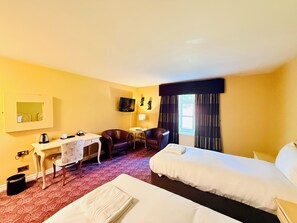 Een hotelkamer met twee bedden, een bureau, een stoel, een televisie en een raam met gordijnen.