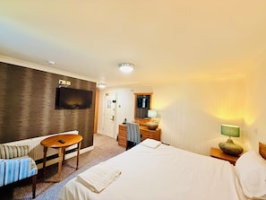 Ein Hotelzimmer mit Bett, Fernseher, Schreibtisch, Stuhl und kleinem Tisch.
