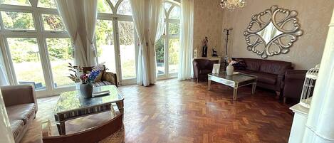 A spacious room with a large window, a chandelier, a sofa, and a coffee table.