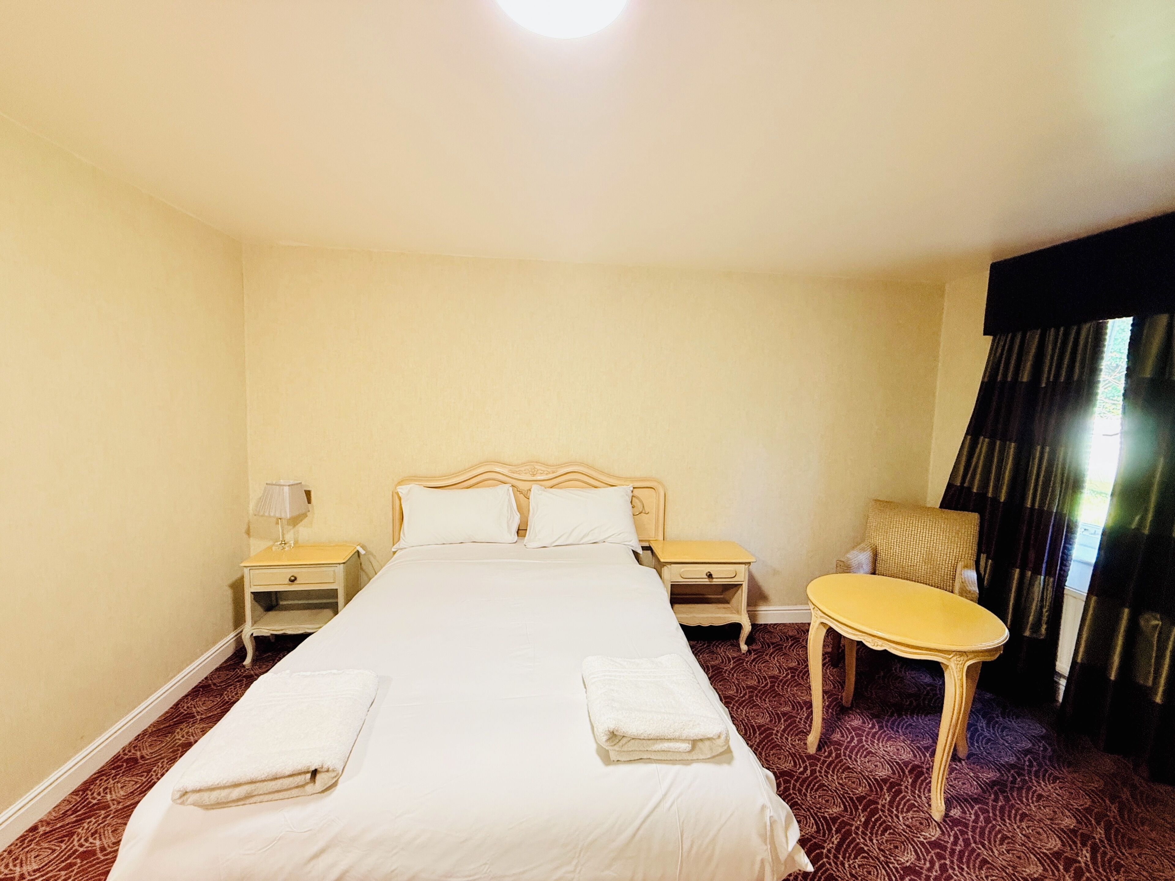 A hotel room with a large bed, two bedside tables, a chair, and a small table.