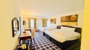A hotel room with two beds, a desk, a chair, a table with a kettle, and a check-in trolley.