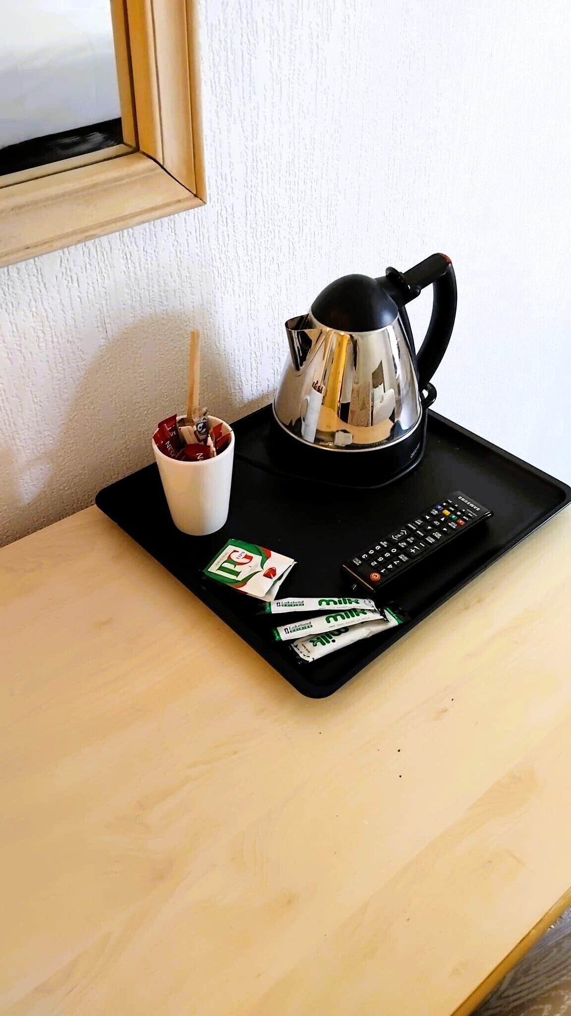 A coffee maker, a mug, a remote control, and some snacks on a tray.
