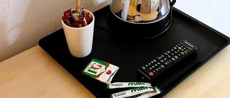 A coffee maker, a mug, a remote control, and some snacks on a tray.