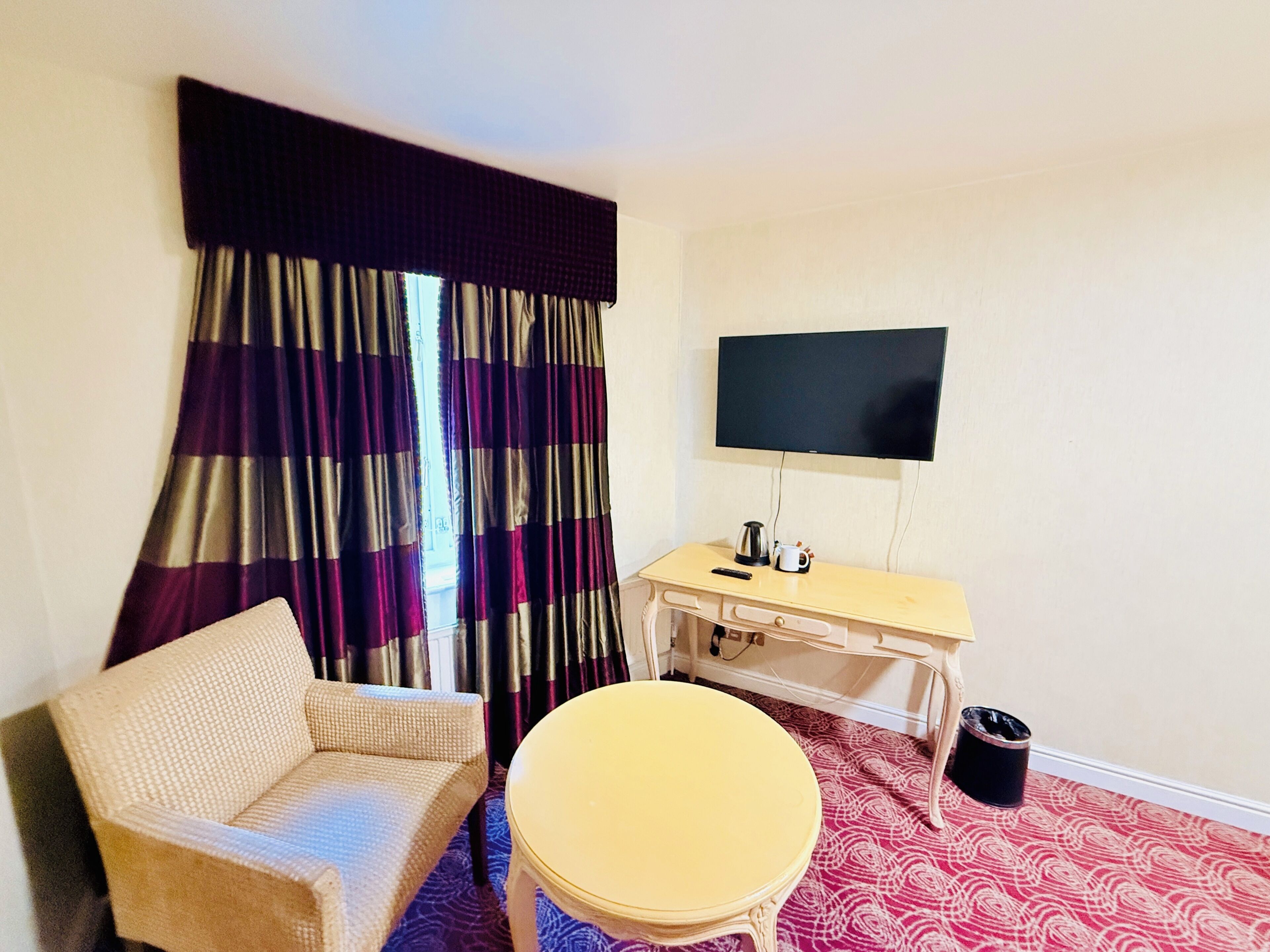Ein Zimmer mit einer Couch, einem kleinen runden Tisch, einem Fernseher und einem Fenster mit Vorhängen.