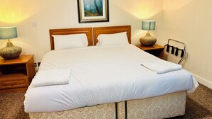 Una cama bien hecha con sábanas blancas, dos mesitas de noche con lámparas, un cabecero y un cuadro en la pared.