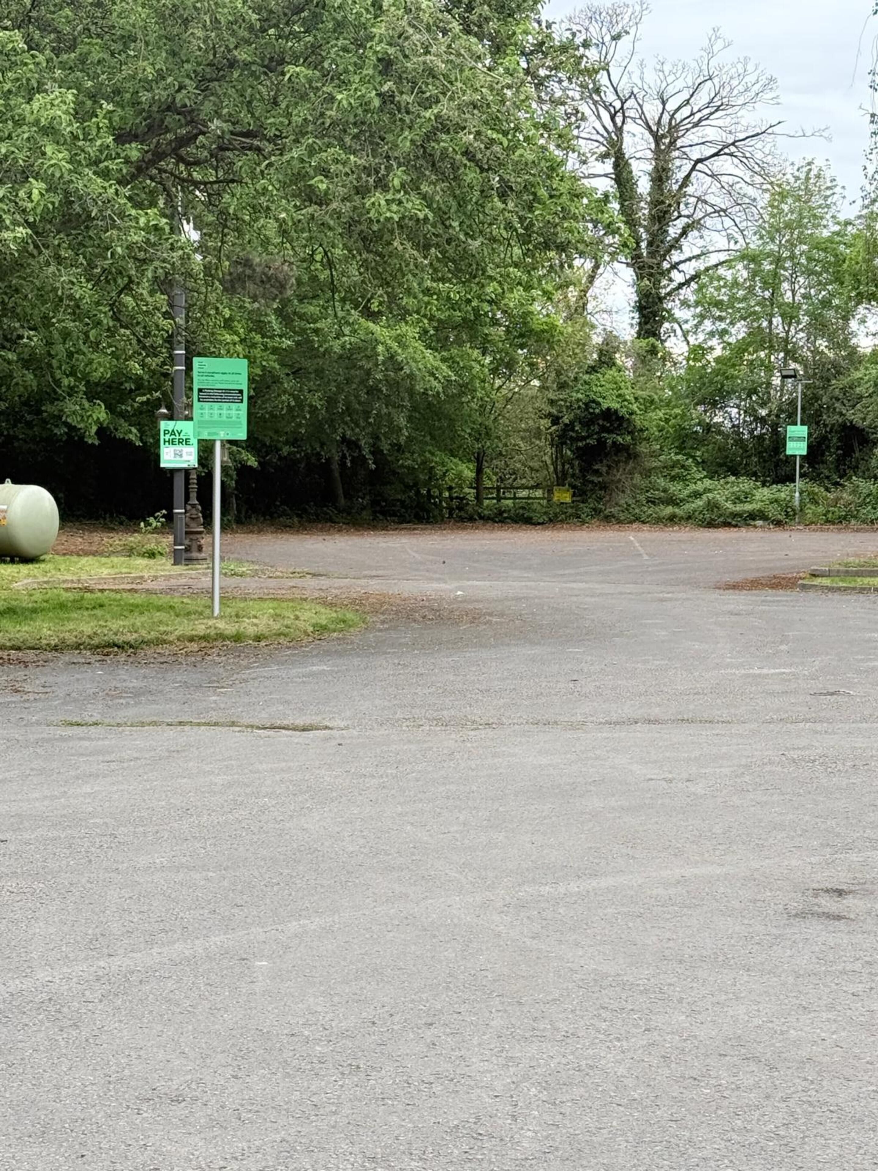A parking area with green signs, a paved surface, and trees in the background.
