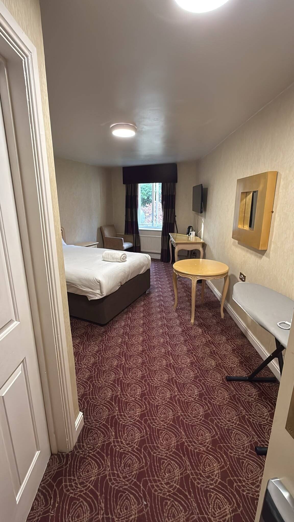 Habitación de hotel con cama, una mesita, una silla, un escritorio y un televisor.