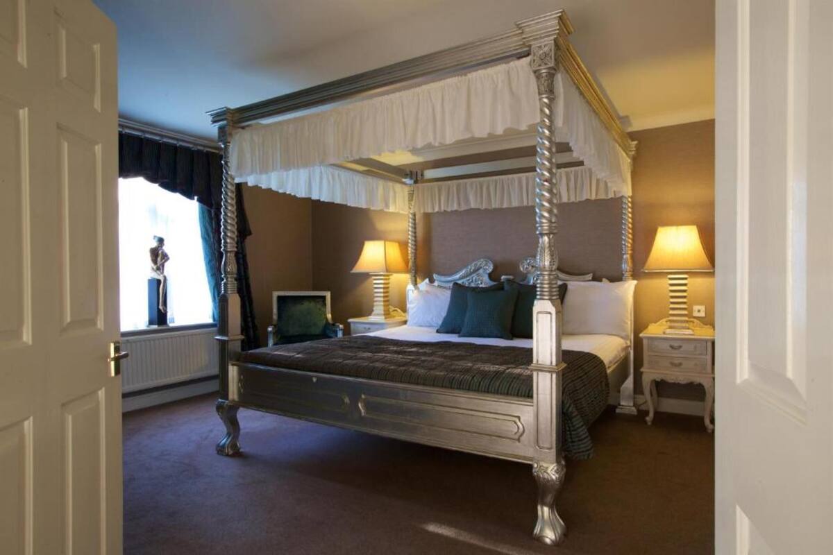 A four-poster bed with a canopy, bedside tables, lamps, and a window with curtains.