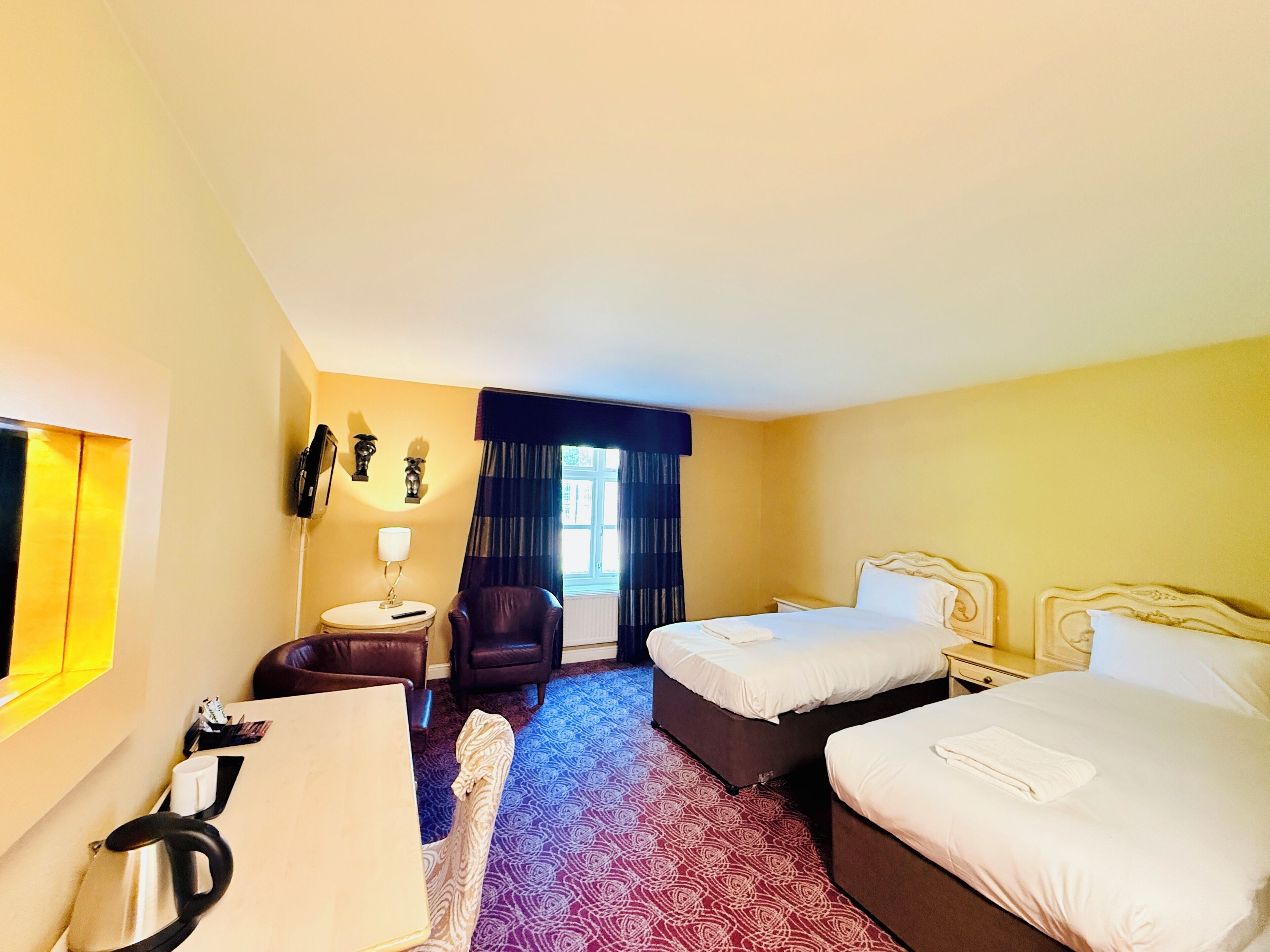 Une chambre d’hôtel avec deux lits, un bureau, une chaise, une lampe et une fenêtre avec des rideaux.