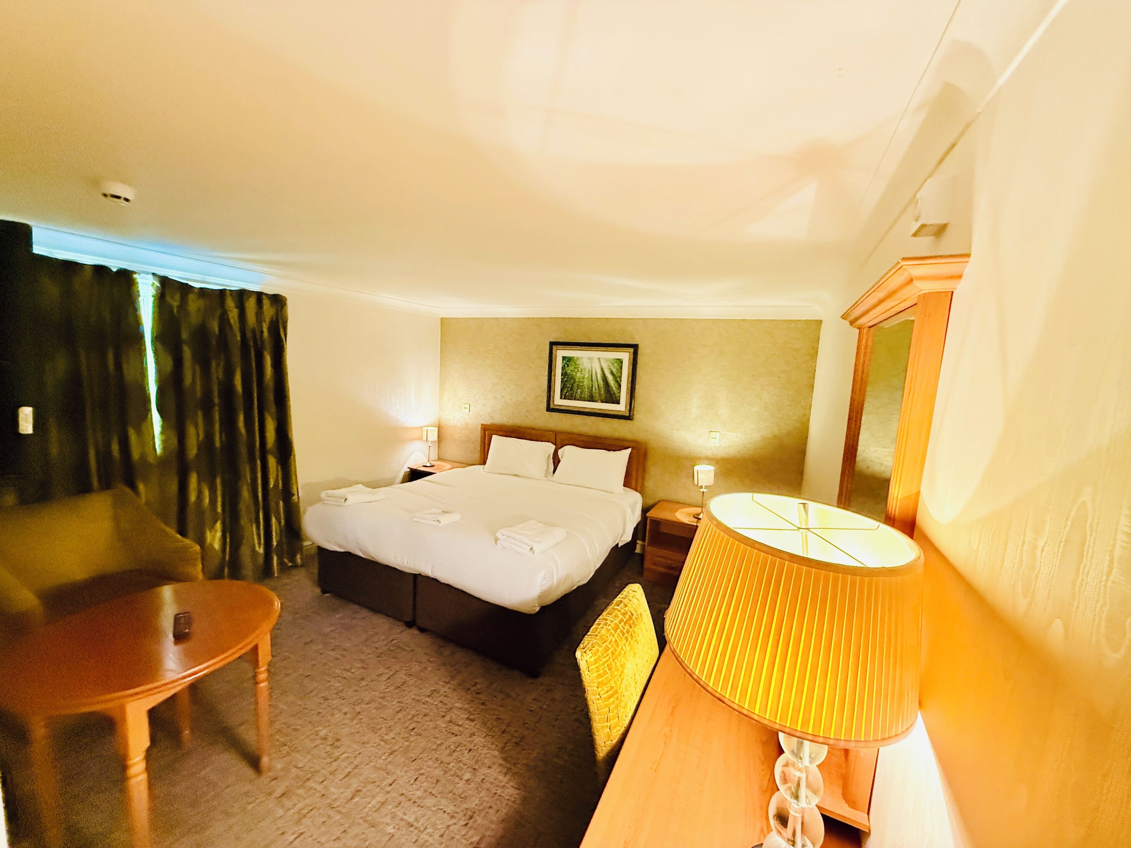 A hotel room with a bed, a desk, a chair, a lamp, and a painting on the wall.