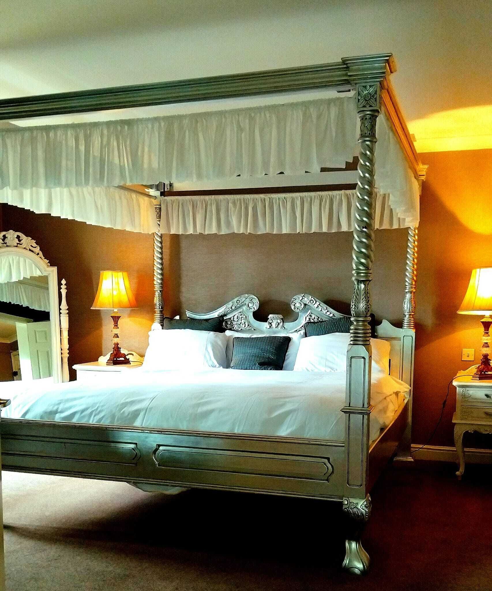 A four-poster bed with a canopy, two bedside lamps, and a mirror on the left.
