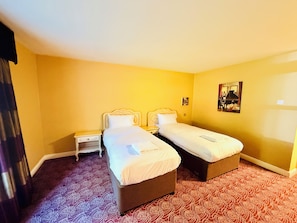Una habitación de hotel con dos camas, una mesita de noche y una alfombra estampada.