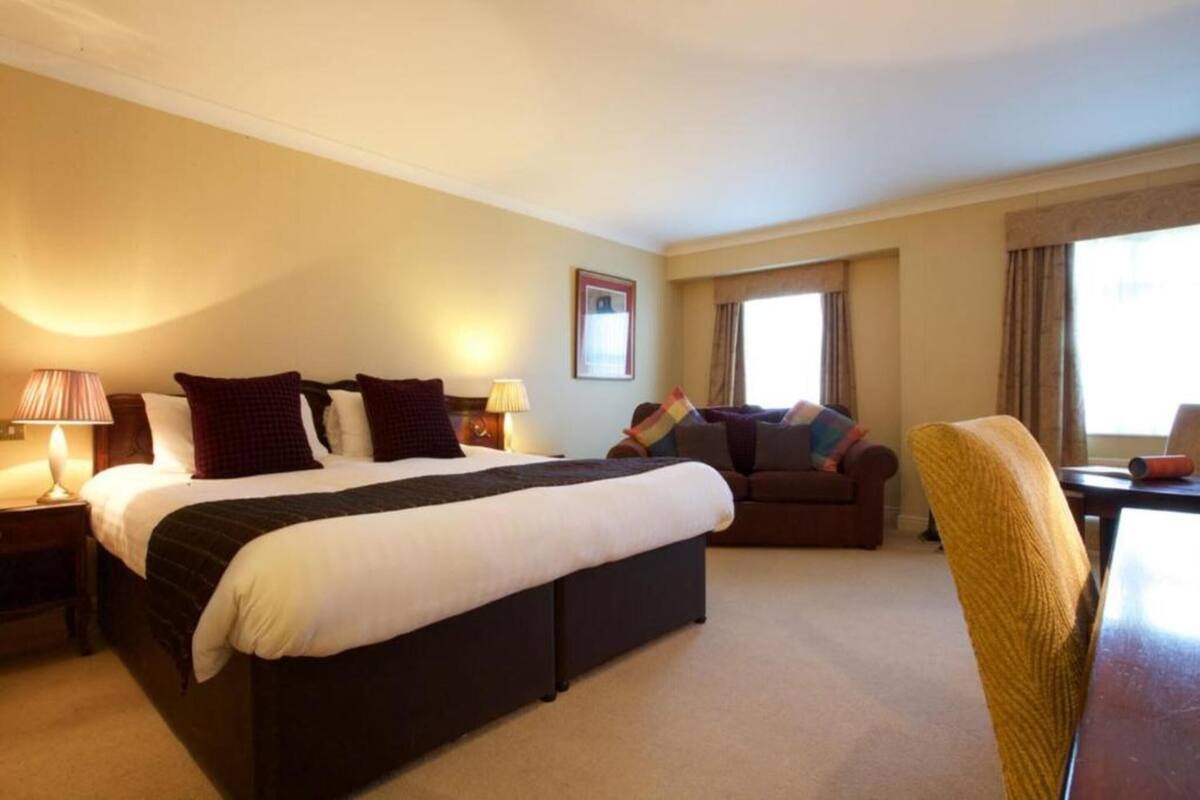 A hotel room with a large bed, a sofa, a dining table, and a chair.