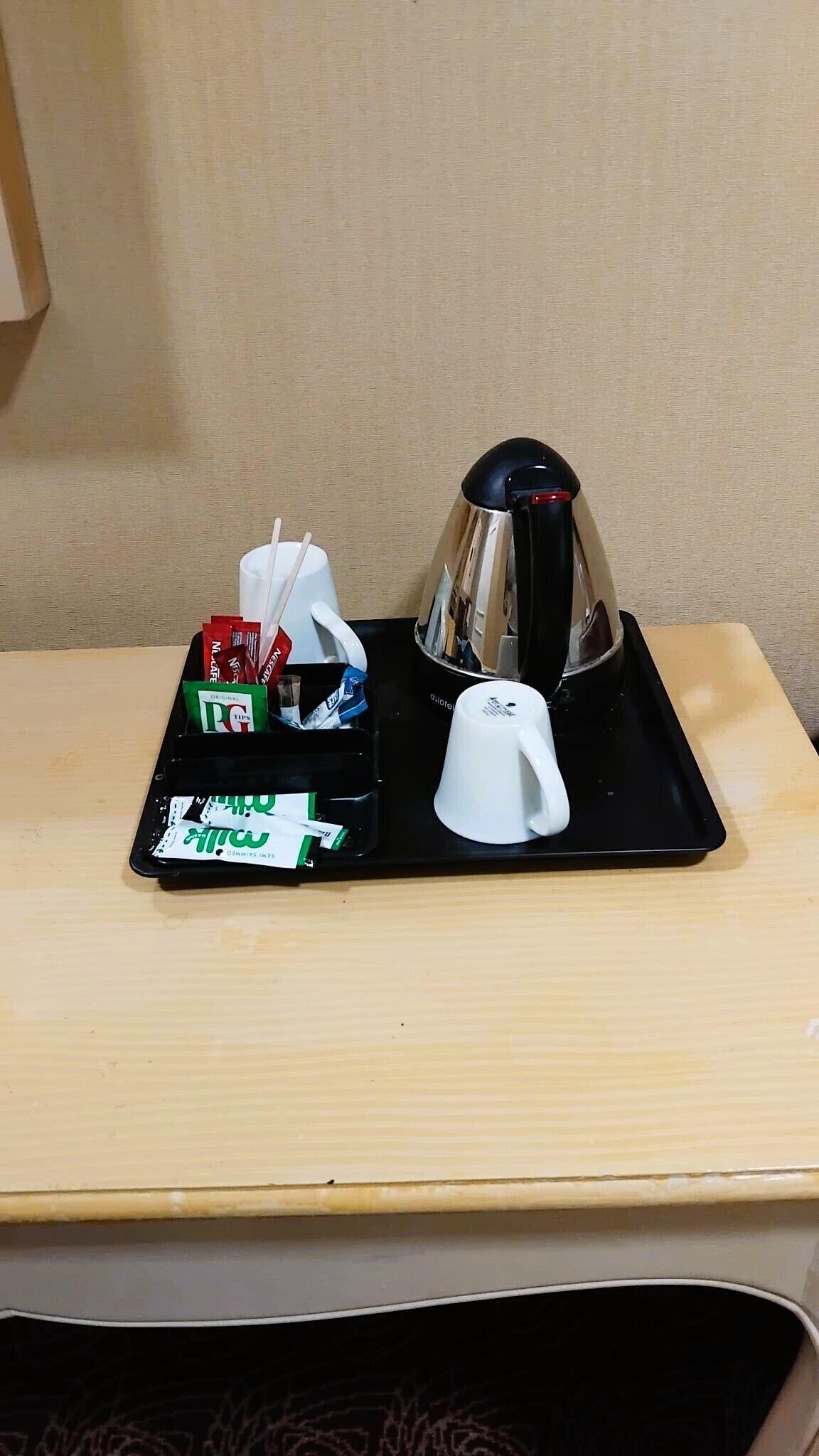 Una bandeja con cafetera, una taza blanca y un juego de vasos desechables y pañuelos.
