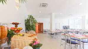 A spacious dining area with multiple tables and chairs, a large potted plant, and a television screen.