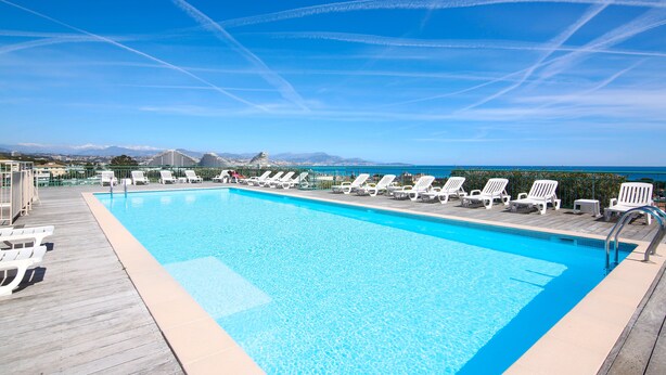 A clear blue sky with contrails, a swimming pool with lounge chairs, and a view of mountains in the distance.