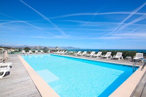 A clear blue sky with contrails, a swimming pool with lounge chairs, and a view of mountains in the distance.