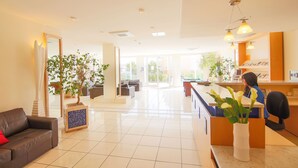 A modern hotel lobby with a reception desk, seating area, and potted plants.