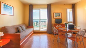 A room with a sofa, a dining table with chairs, a laptop, and a TV.