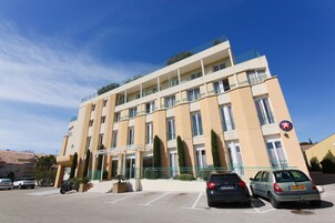 Un hotel de varios pisos con balcones, un estacionamiento y un cielo azul despejado.