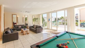 A pool area with two sofas, a pool table, and large windows offering a view of the outside.