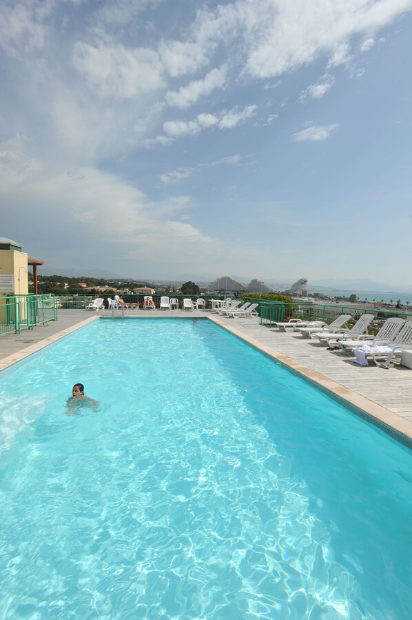 A swimming pool with clear blue water, surrounded by lounge chairs and a view of distant mountains.