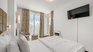 A hotel room with a large bed, a flat-screen TV mounted on the wall, a chair, and a small table. - Hotel ANTARES (Bratislava)